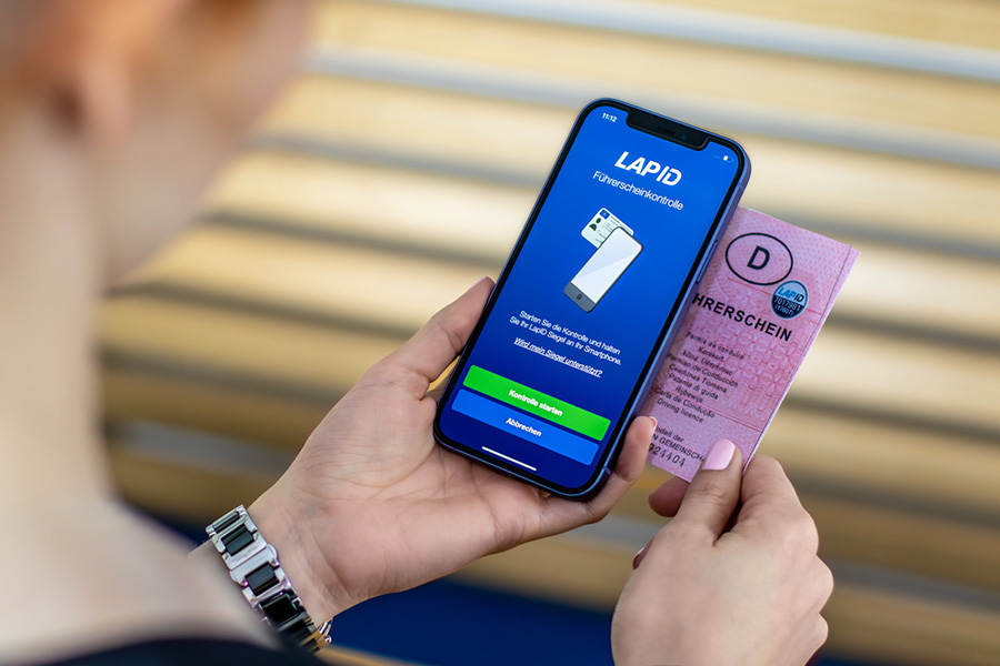 Eine Frau nutzt die Smartphone-App für die LapID Führerscheinkontrolle, um ihre Fahrerlaubnis mit dem LapID NFC-Tag zu scannen. Dies zeigt die nahtlose Kommunikation zwischen den Anwendungen der Carano Software und LapID.